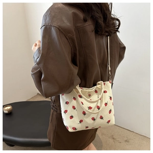 Detail of strawberry embroidery on off-white corduroy tote worn with a leather jacket