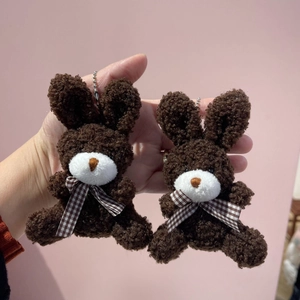 Close-up of two small brown plush bunny charms with checkered bowties on pink background