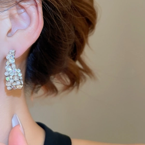 Close-up of elegant C-shaped silver earrings with sparkling crystals and white pearls