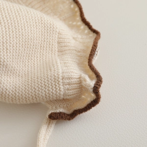 Close-up of baby knit hat with cream fabric, brown wavy edges and detailed textures