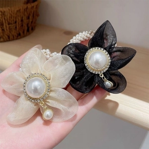 Détail de chouchous fleurs en organza élégants avec strass et perles en doré et noir