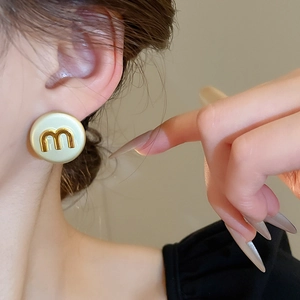 Macro shot of circular cream ear studs with gold M letter logo detail on ear