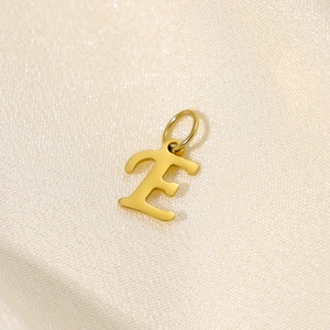 Macro shot of gold stainless steel letter E pendant on a smooth silk fabric background