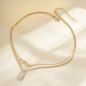 Close-up of golden double-layer stainless steel necklace with rectangular shell pendant