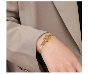 Polished gold belt buckle bracelet worn over a brown suit sleeve for a luxury look