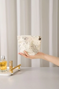 Detail of the chic beige makeup bag with black bow and gold flower zipper pull