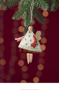 Detail of hand-painted angel ornament on pine branch with warm bokeh holiday lighting