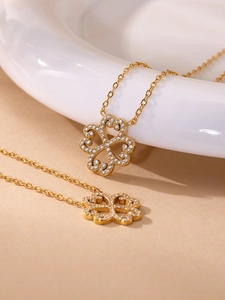 Detail view of two gold clover necklaces featuring pavé rhinestones on a beige surface