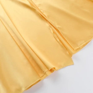 Detail view of bright yellow satin dress hem showing fine stitching and draped silk texture