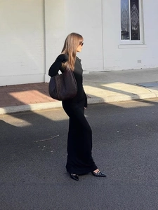 Femme élégante en robe noire à épaules dénudées avec un sac à bandoulière en cuir tressé