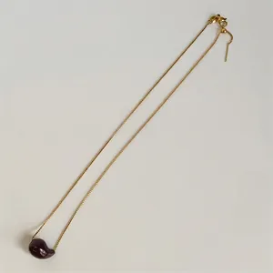 Macro detail of gold-plated square box chain and deep red teardrop pendant with lobster clasp