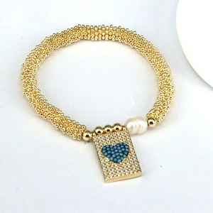 Detail view of a gold beaded bracelet with a blue heart pendant and zircon accents