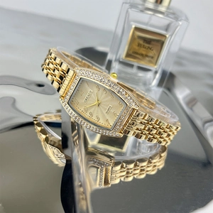 Detailed view of tonneau gold watch with emerald dial and rhinestone bezel on reflective surface