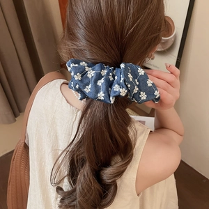 Detail of dark blue denim scrunchie with white flower embroidery on a ponytail