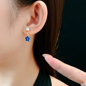 Close-up of model wearing white pearl stud and blue four-petal flower dangle earring