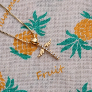 Close-up of golden cross necklace with wings and gemstones on pineapple patterned fabric