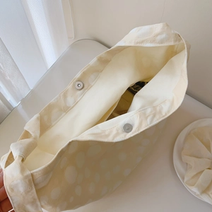 Detail view of the metal magnetic clasps and white lining of the pale yellow polka dot tote