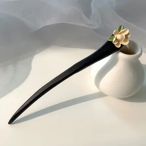 Detailed close-up of a black wooden hair pin with cream flower and green leaves decoration