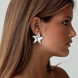 Close-up of star-shaped silver steel earring on model with metallic finish and studs
