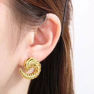Close-up of golden irregular spiral horn earrings worn on ear with high-gloss finish