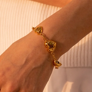 Detailed close-up of a gold hollow heart bracelet on a wrist with three heart charms
