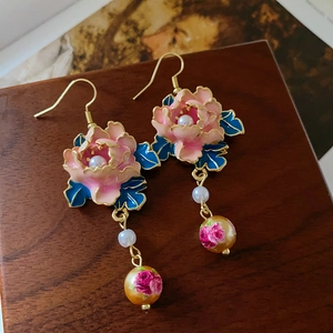 Detail von Vintage-Ohrringen mit Emaille-Blumen und hängenden Perlen auf einer Holzfläche
