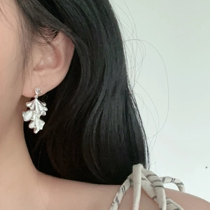 Macro shot of silver pleated leaf earrings worn by a model in soft lighting