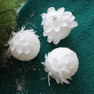Three white petal-style Christmas ornaments with glitter on a dark green velvet background