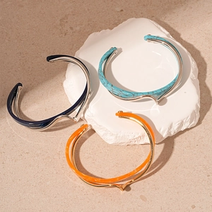 Close-up of double-layered enamel cuffs in blue, green and orange on stone display