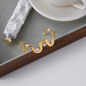 Detailed view of a wave-shaped 18K gold stainless steel bangle with three clear zircons