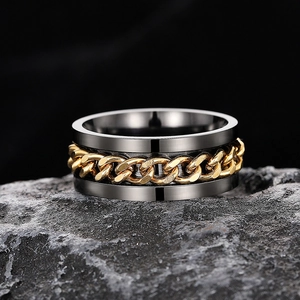 Macro shot of gunmetal spinner ring with golden Cuban chain on a textured stone