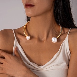 Detail of gold metal choker with textured ridges and large pearls on a female neck
