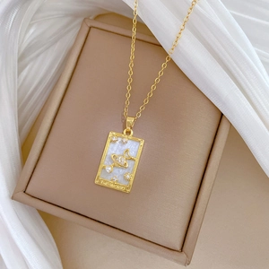 Titanium steel Tarot necklace with gold Saturn and pearl pendant on a beige jewelry box