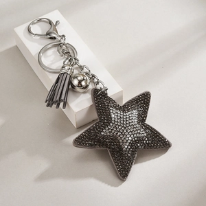 Detail shot of a star keychain with dark grey rhinestones and leather fringe on a white block