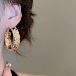 Close-up of golden textured hoop earrings on a model showing elegant metallic details
