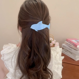 Detail view of blue whale hair claw clip styled on blonde hair in a cozy home setting