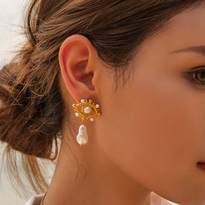 Detailed close-up of eye-shaped gold earrings with baroque pearls worn by a model