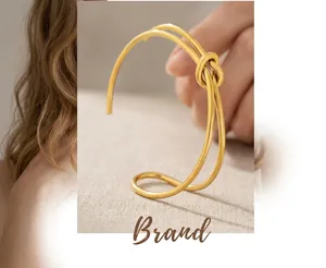Detail of a minimalist gold knotted open cuff bracelet on a white textured background