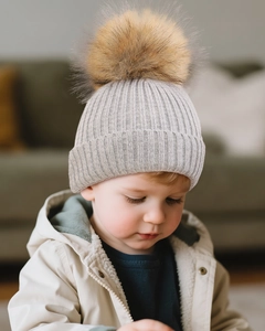 Detail view of child wearing a light grey ribbed knit beanie with brown faux fur pom-pom