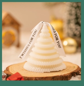 Close-up of white origami Christmas tree candle with WISHES FOR YOU ribbon on wood