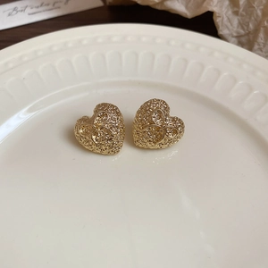 Detailed close-up of golden heart-shaped stud earrings with textured bow design