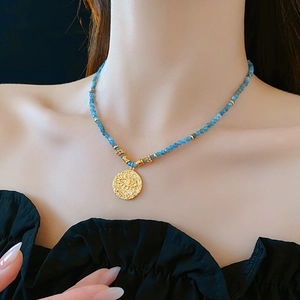 Close-up of ethnic beaded necklace with blue beads and a gold evil eye pendant charm