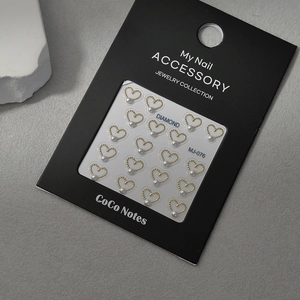 Macro detail of gold heart-shaped nail art charms with white pearls on a display card
