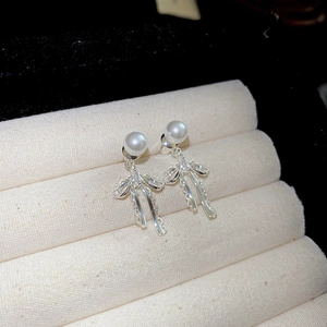 Close-up of silver bow earrings with pearl center and fringe drop on a jewelry stand