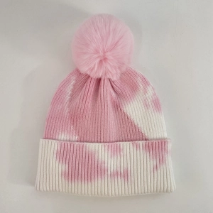 Detail of pink tie-dye knit beanie featuring a soft faux fur pom-pom and ribbed cuff