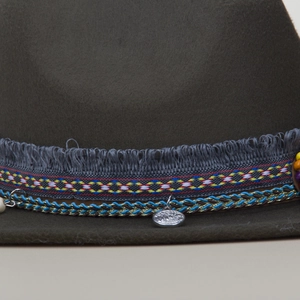 Detail of dark green fedora with bohemian fringe ribbon and silver pendant accent