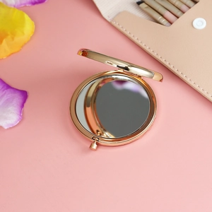 Close-up of a round gold portable compact mirror opened on a soft pink background