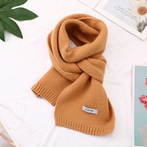 Close-up of ginger yellow knitted scarf with soft wool texture and minimal logo label