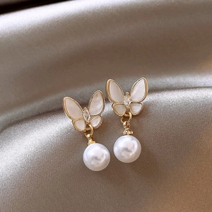 Detail of gold butterfly earrings with white wings and hanging pearl on silk background