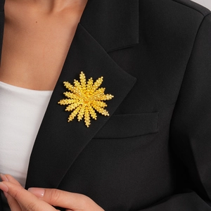 Detail of a golden floral sunburst brooch pinned on a black tailored suit jacket